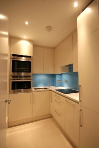 Simple spray-painted Kitchen within a confined space.  Vibrant blue glass splashback and stone worktop.