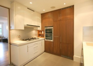 Kitchen made from a combination of spray-painted and Walnut veneered cabinets. Stone worksurfaces and neutral glass splashback.