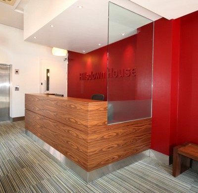 Reception Desk made from American Black Walnut veneer with stainless steel plinth and glass panel.